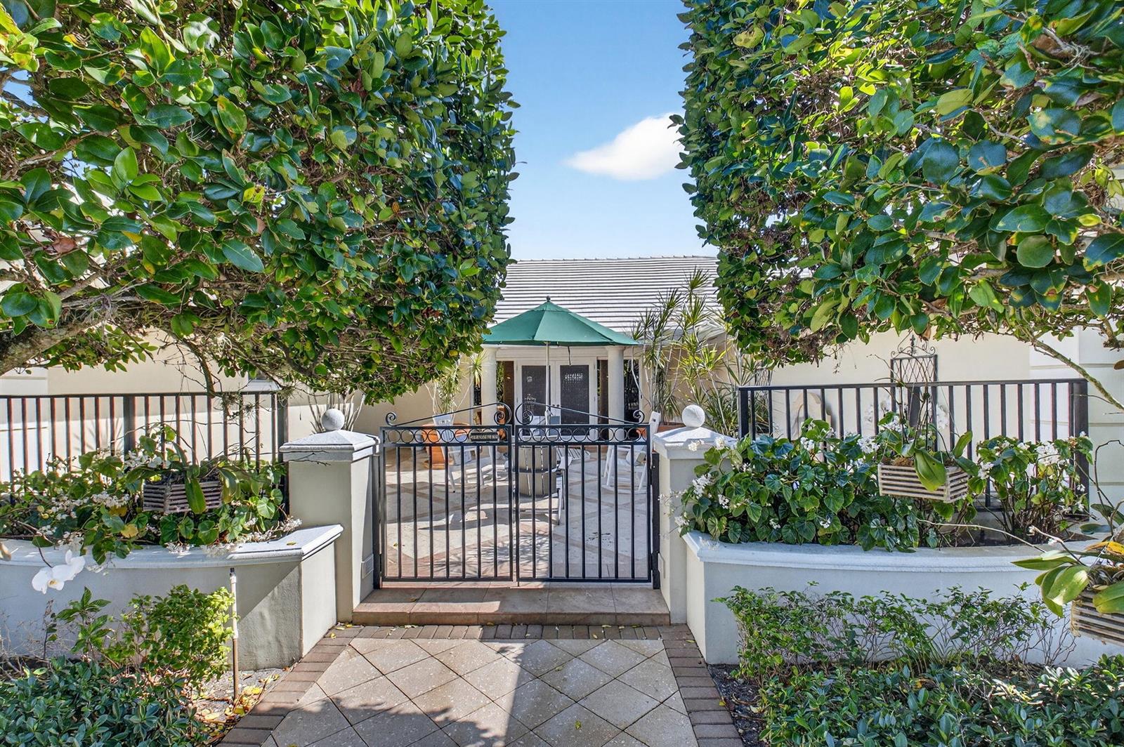 A gated entryway leads to a paved patio with a green umbrella and house entrance — 11740 N Lake Drive, Boynton Beach FL 33436, BOYNTON BEACH, FL