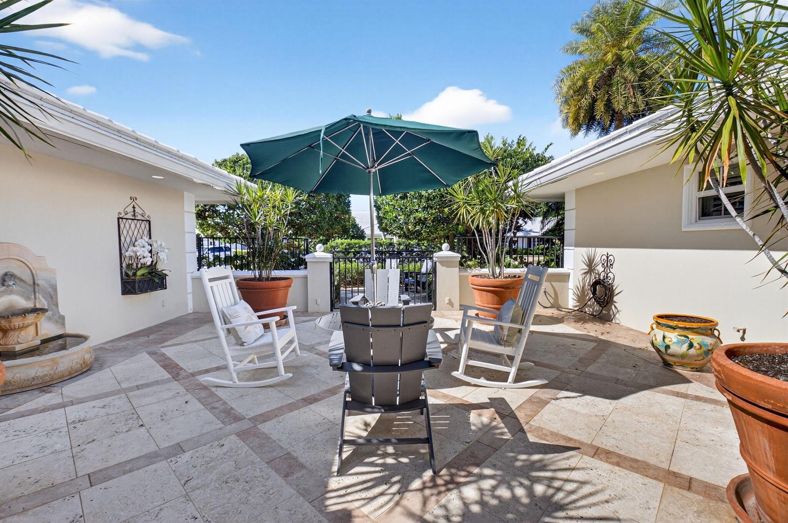 A patio features a green umbrella, three chairs, potted plants, and a stone fountain — 11740 N Lake Drive, Boynton Beach FL 33436, BOYNTON BEACH, FL