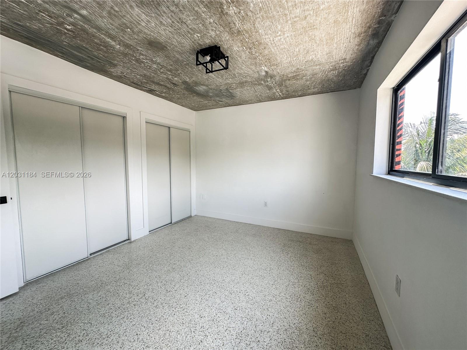 A bedroom features a raw concrete ceiling, white walls, sliding closet doors, and speckled flooring — 190 NW 69th St # 8, Miami FL 33150, MIAMI, FL