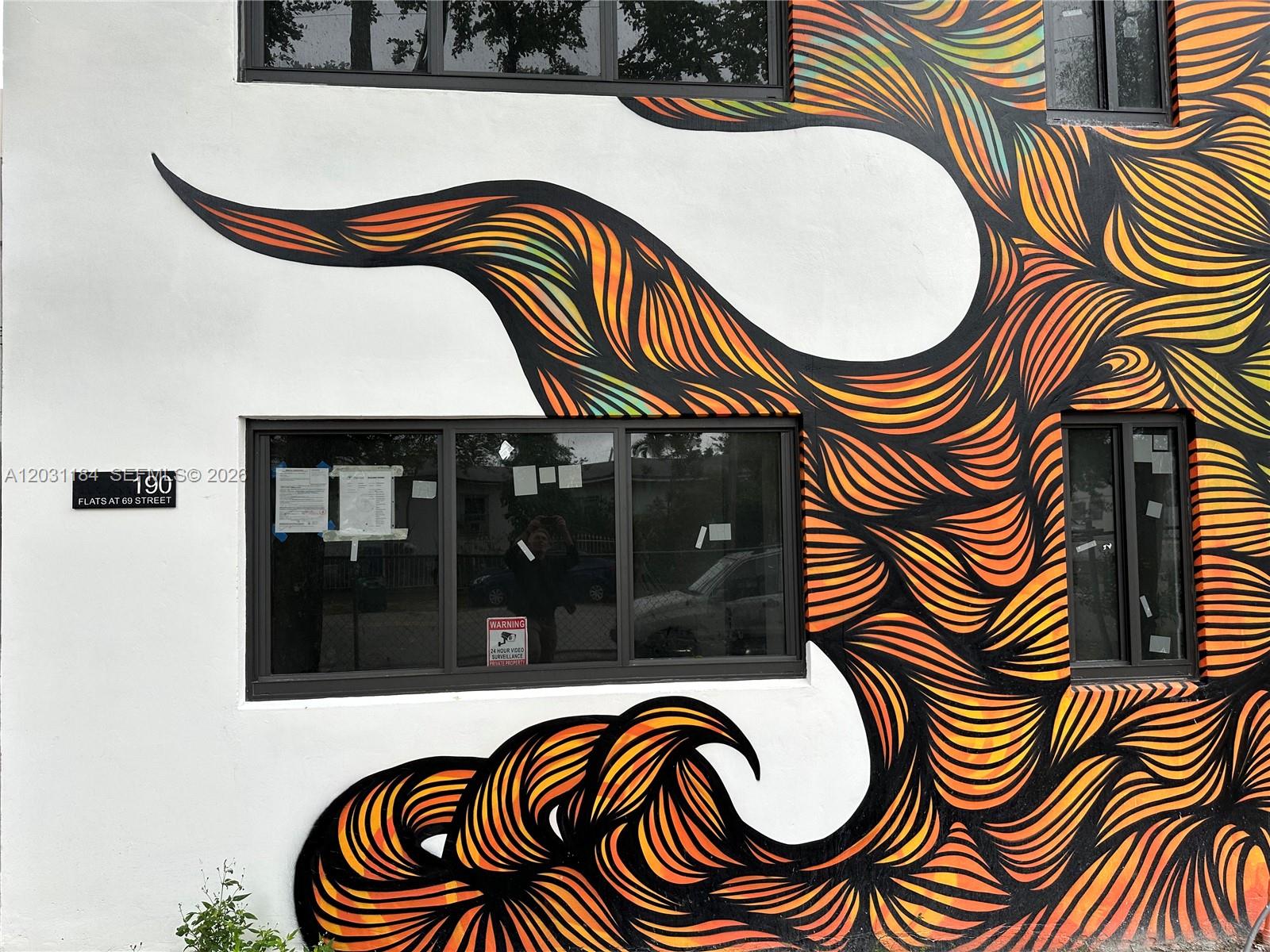 A white exterior wall features a large, colorful abstract mural and several dark-framed windows — 190 NW 69th St # 8, Miami FL 33150, MIAMI, FL