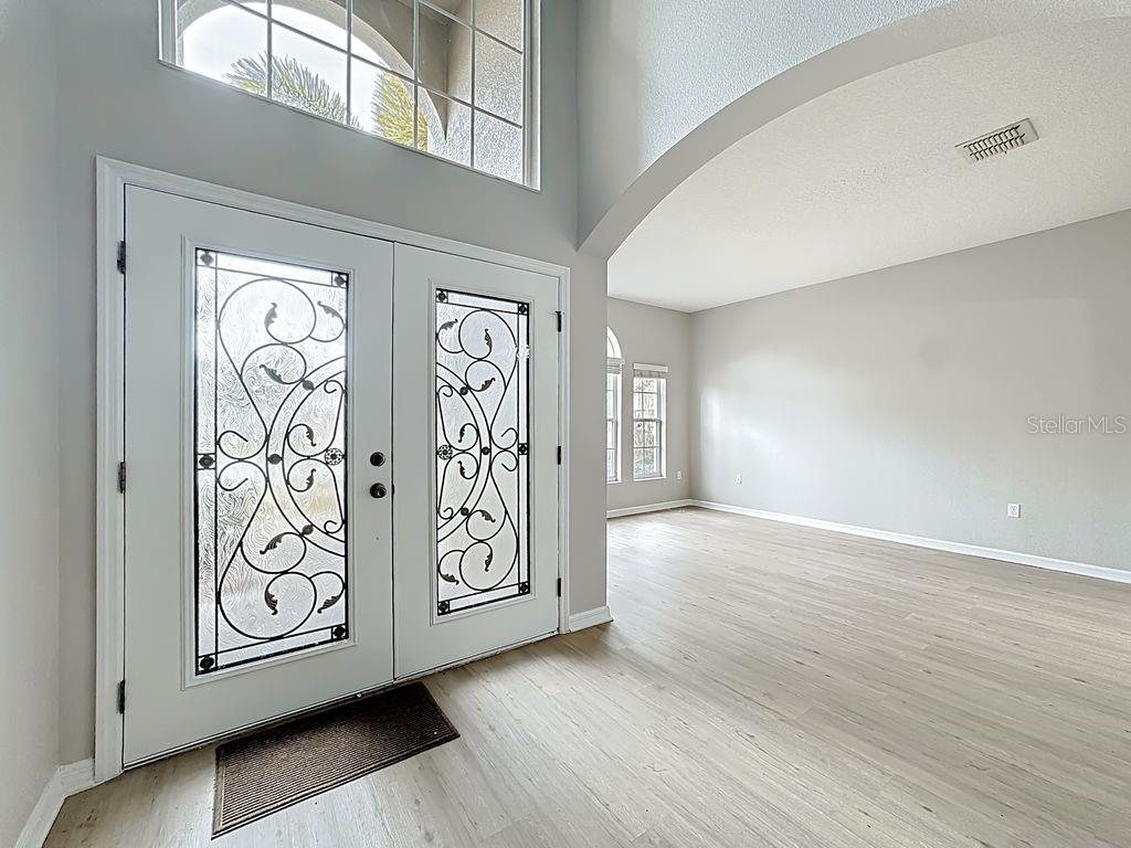 An entryway with light wood-look flooring, a double front door with decorative glass, and high ceilings — 15612 MONTESINO DRIVE, ORLANDO, FL