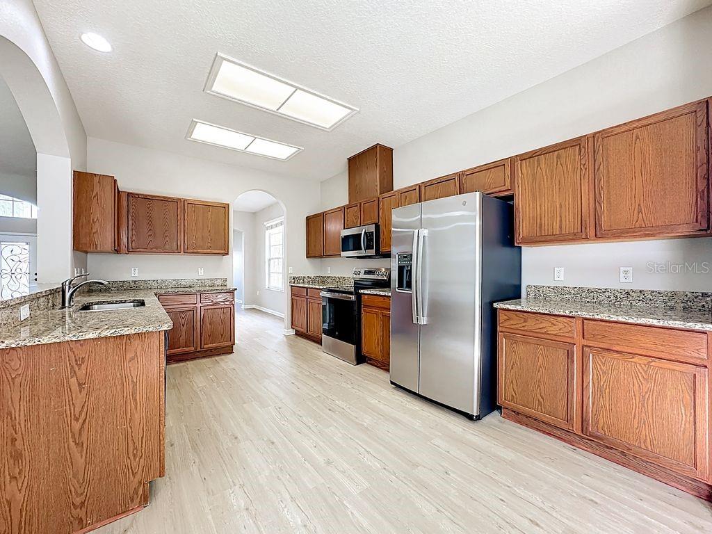 A kitchen with wood cabinets, granite countertops, stainless steel appliances, and light-colored wood-look flooring — 15612 MONTESINO DRIVE, ORLANDO, FL