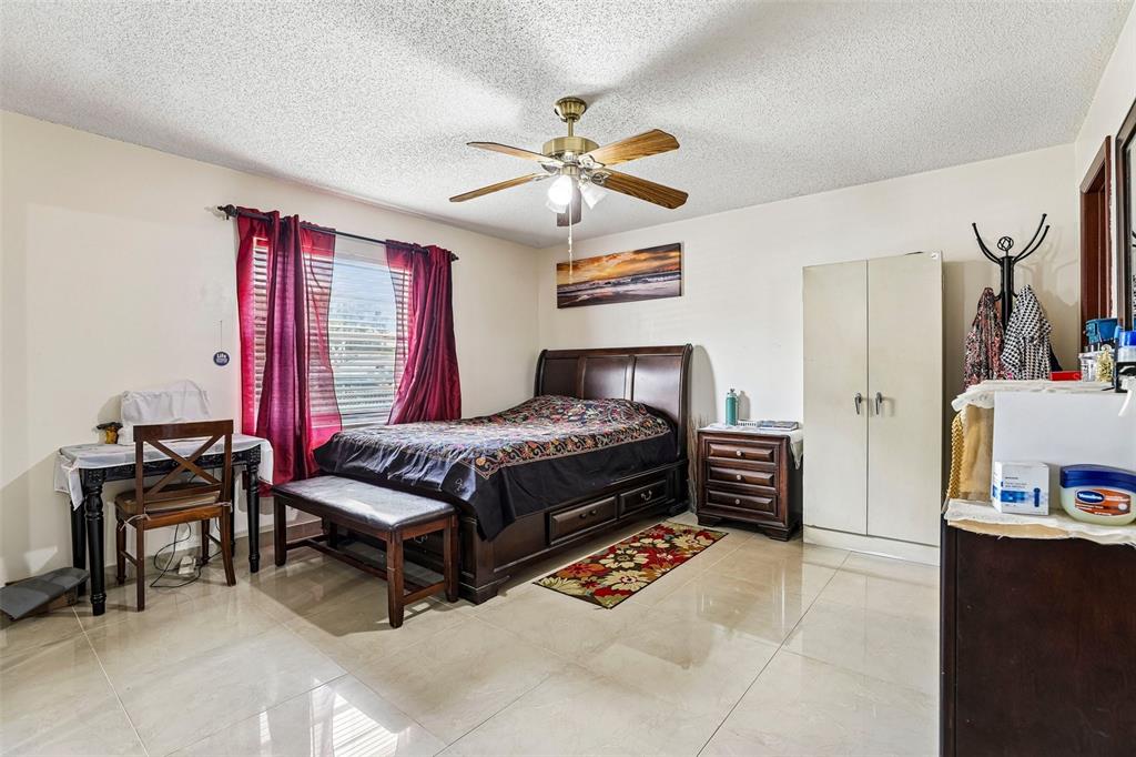 A bedroom features a dark wood bed, tile flooring, a ceiling fan, and red curtains — 1320 MILL CREEK PLACE, KISSIMMEE, FL