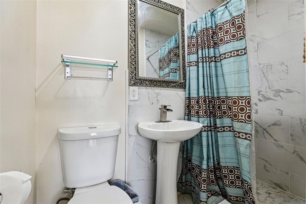 A bathroom features a pedestal sink, a toilet, a glass shelf, and a patterned shower curtain — 1320 MILL CREEK PLACE, KISSIMMEE, FL