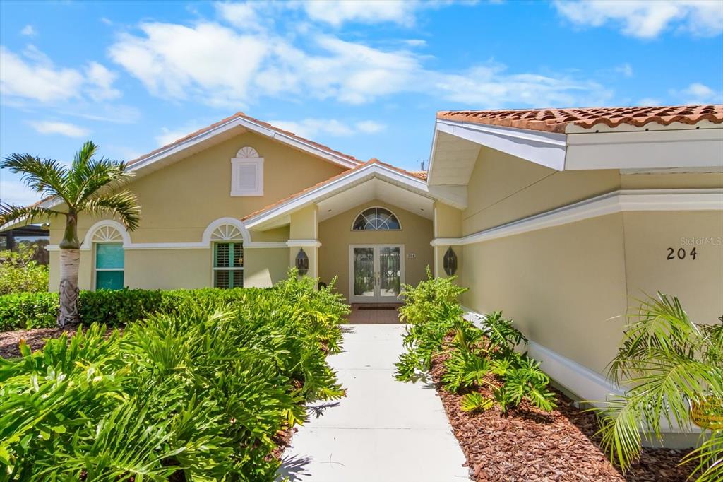 A tan house with a tile roof, palm tree, and a walkway leading to the entrance — 204 WINDWARD DRIVE, OSPREY, FL