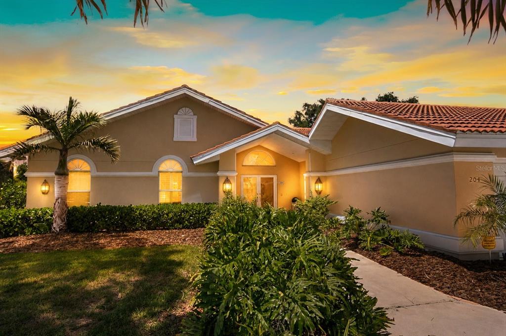 A single-story house with a tiled roof, arched windows, and a palm tree at sunset — 204 WINDWARD DRIVE, OSPREY, FL