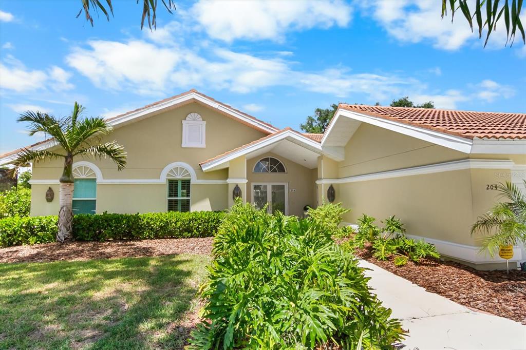The exterior of a single-story house features a tan stucco facade and a tiled roof — 204 WINDWARD DRIVE, OSPREY, FL