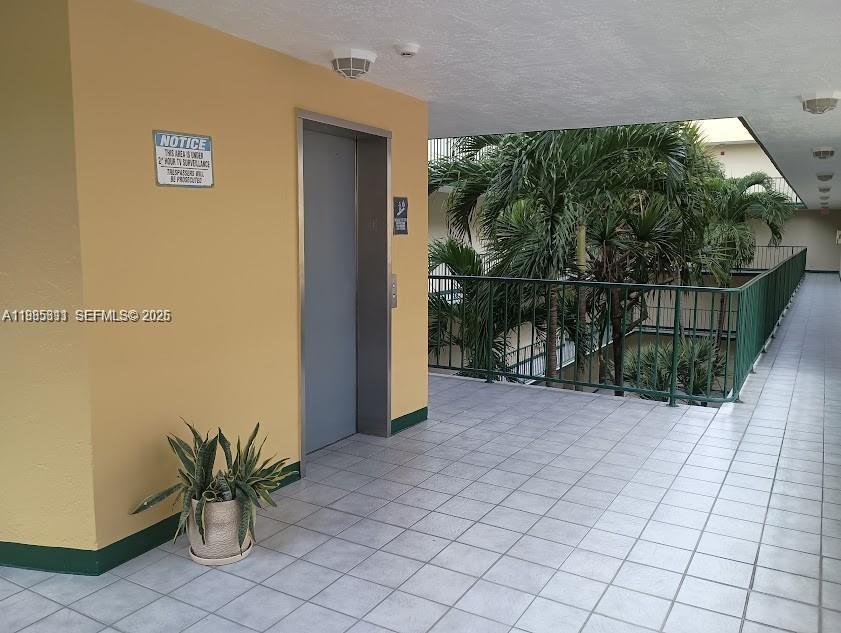 An outdoor apartment hallway features a gray elevator, tiled flooring, and a green metal railing — 8321 NW 7th St # 307, Miami FL 33126, MIAMI, FL