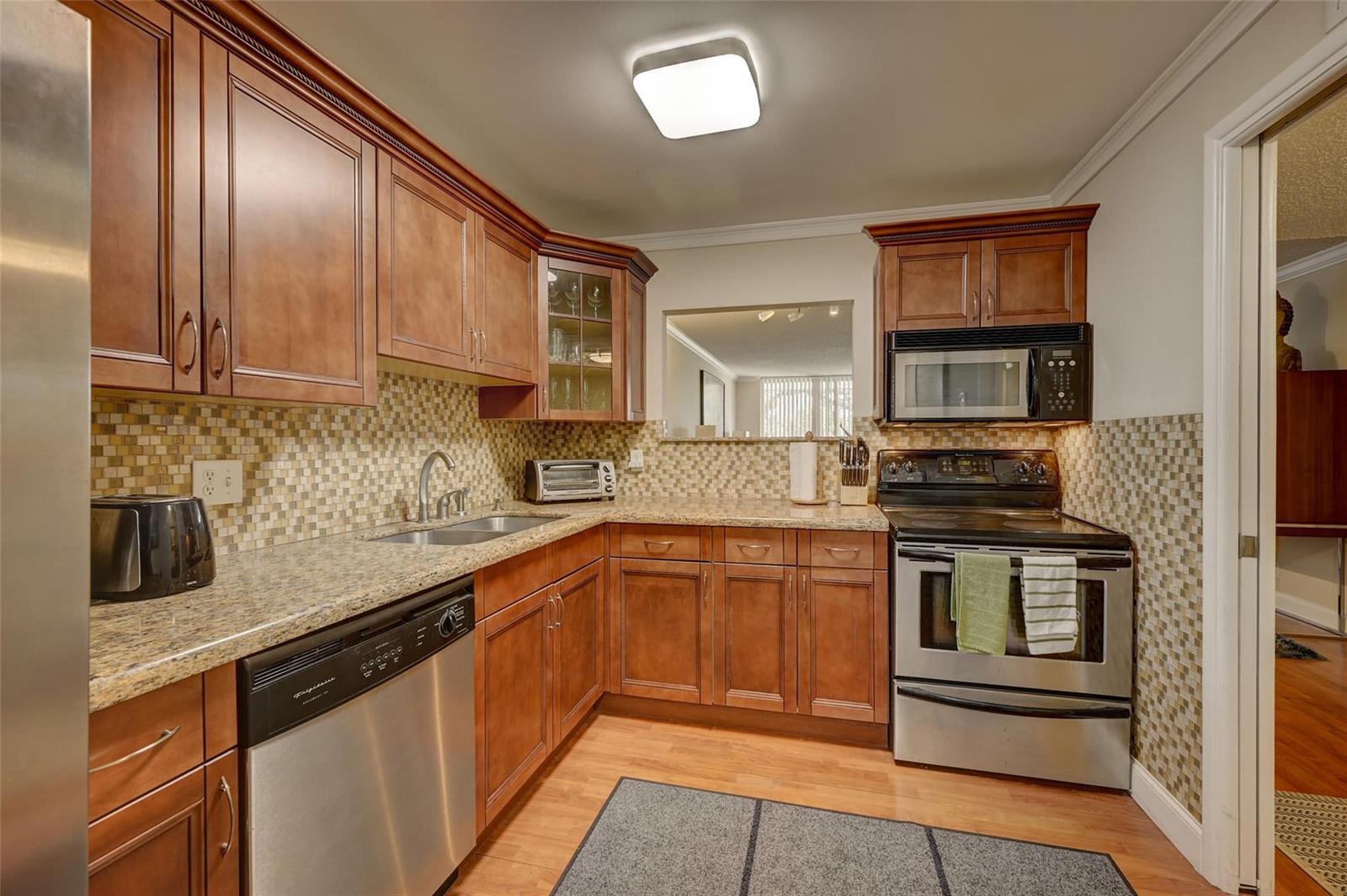 A kitchen with wood cabinets, granite countertops, stainless steel appliances, and a tiled backsplash — 823 Cypress Boulevard # 201, Pompano Beach FL 33069, POMPANO BEACH, FL