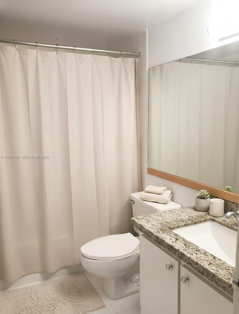 A bathroom features a granite vanity, a white toilet, and a beige shower curtain — 770 Claughton Island Dr # 1216, Miami FL 33131, MIAMI, FL