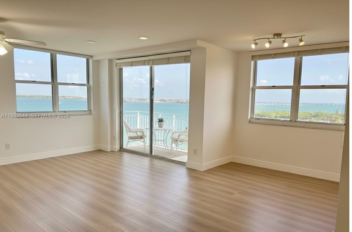 An empty room with light wood-look flooring, large windows, and a balcony overlooking the ocean — 770 Claughton Island Dr # 1216, Miami FL 33131, MIAMI, FL