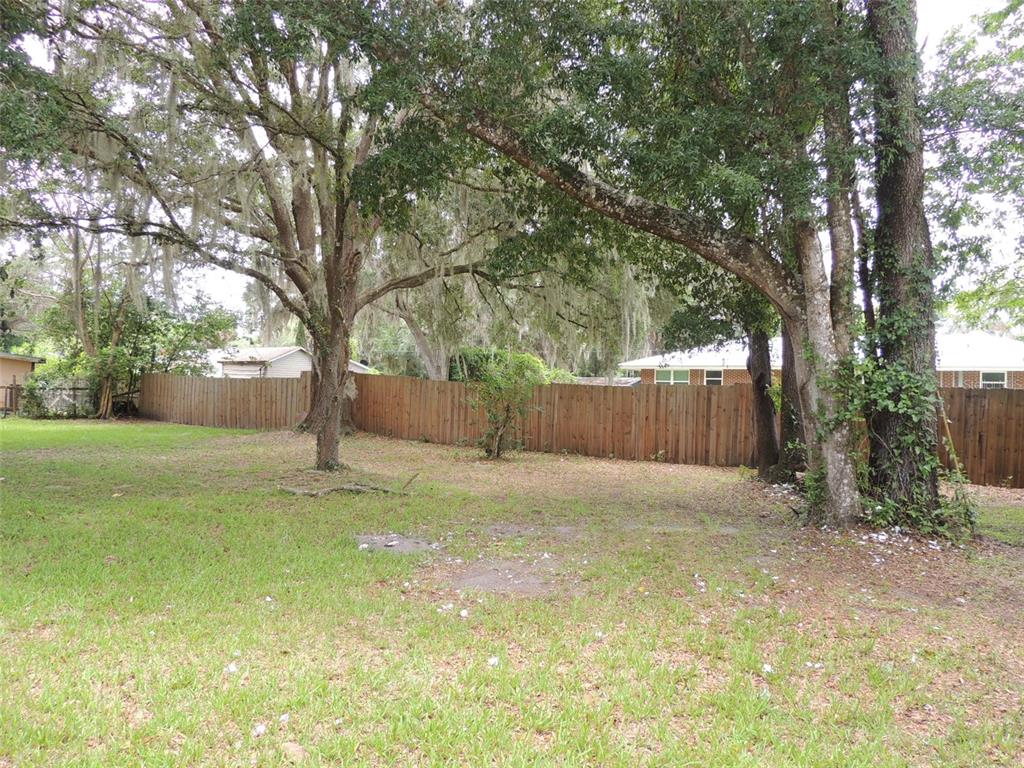 A grassy backyard features mature trees with Spanish moss and a wooden privacy fence — 330 SE 6TH STREET, WILLISTON, FL