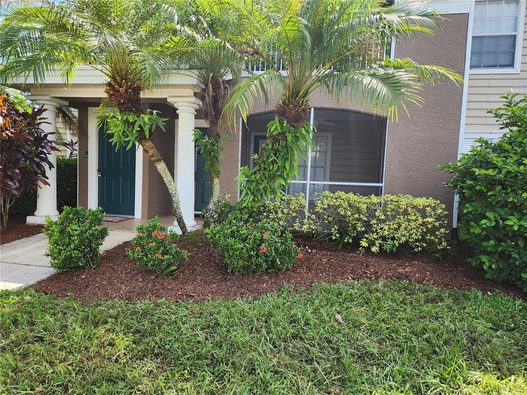 A two-story building exterior features a covered entryway, palm trees, and a screened-in patio — 8933 MANOR LOOP UNIT 105, BRADENTON, FL
