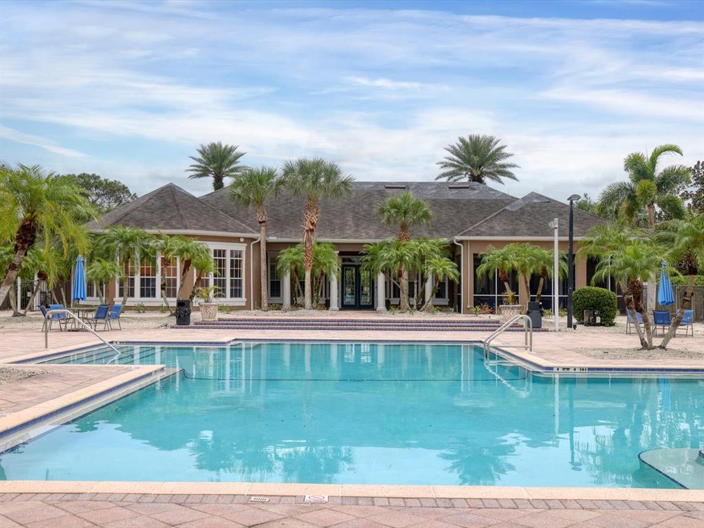 A large swimming pool sits in front of a single-story house with palm trees — 8933 MANOR LOOP UNIT 105, BRADENTON, FL