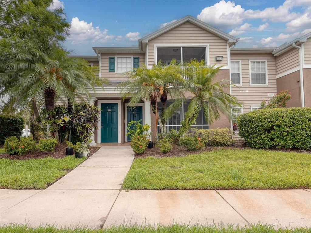 A two-story townhouse exterior with beige siding, a green front door, and palm trees — 8933 MANOR LOOP UNIT 105, BRADENTON, FL