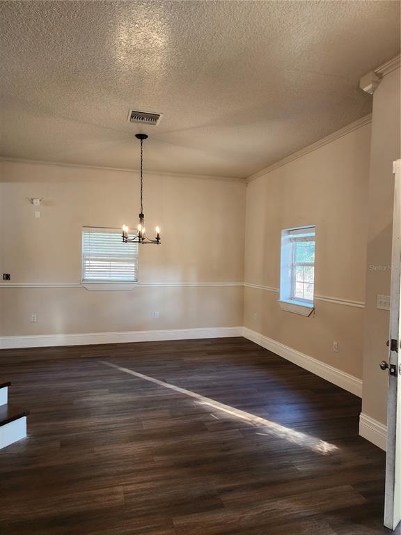 An empty dining room features dark wood-look flooring, beige walls with chair rail molding, and a chandelier — 24247 WOLF BRANCH ROAD, SORRENTO, FL