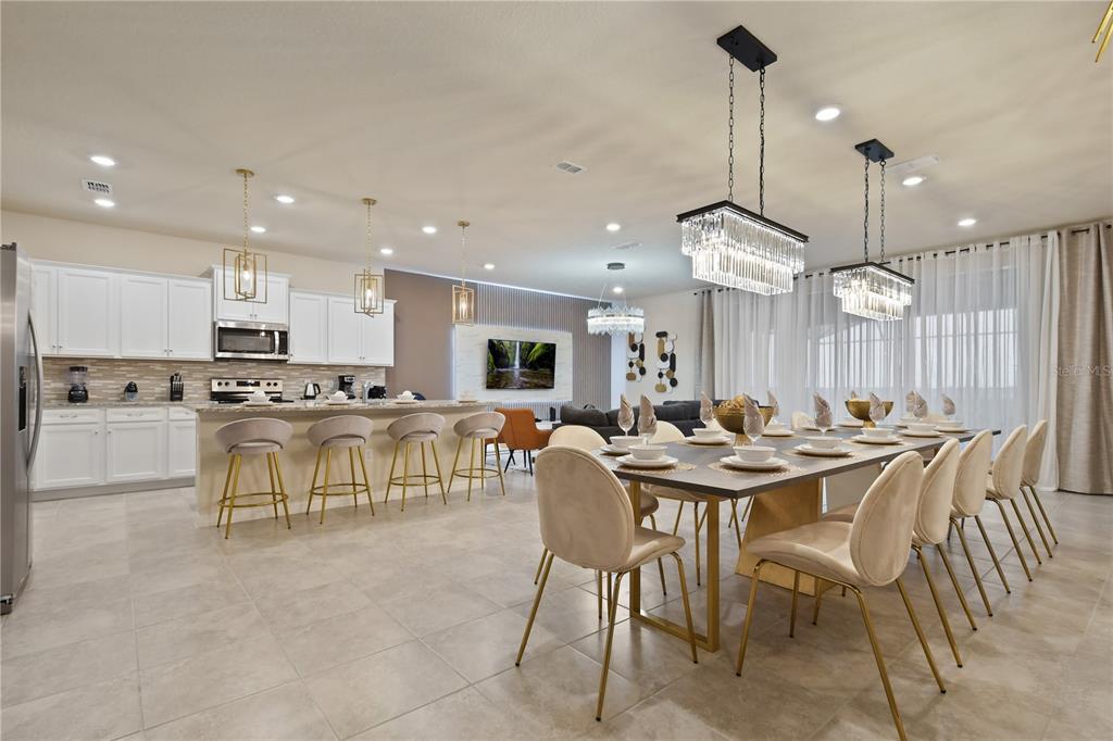 A modern open-concept kitchen and dining area featuring white cabinetry, tile flooring, and crystal chandeliers — 3715 LANA AVENUE, DAVENPORT, FL