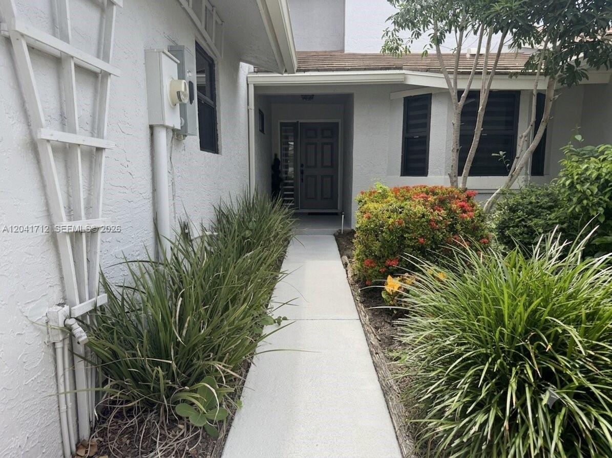 A concrete walkway leads to the front entrance of a house with white stucco walls — 643 Deer Creek North Shore Dr, Deerfield Beach FL 33442, DEERFIELD BEACH, FL
