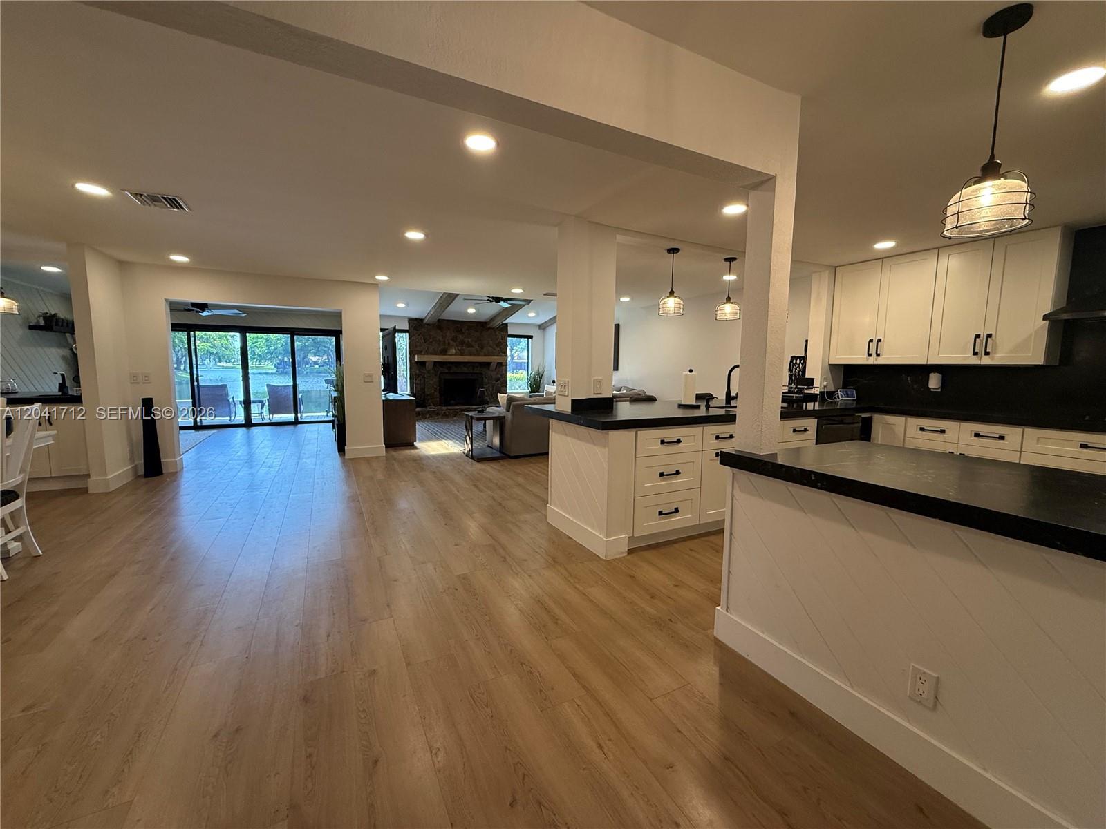 An open-concept kitchen and living area features white cabinets, dark countertops, and wood flooring — 643 Deer Creek North Shore Dr, Deerfield Beach FL 33442, DEERFIELD BEACH, FL