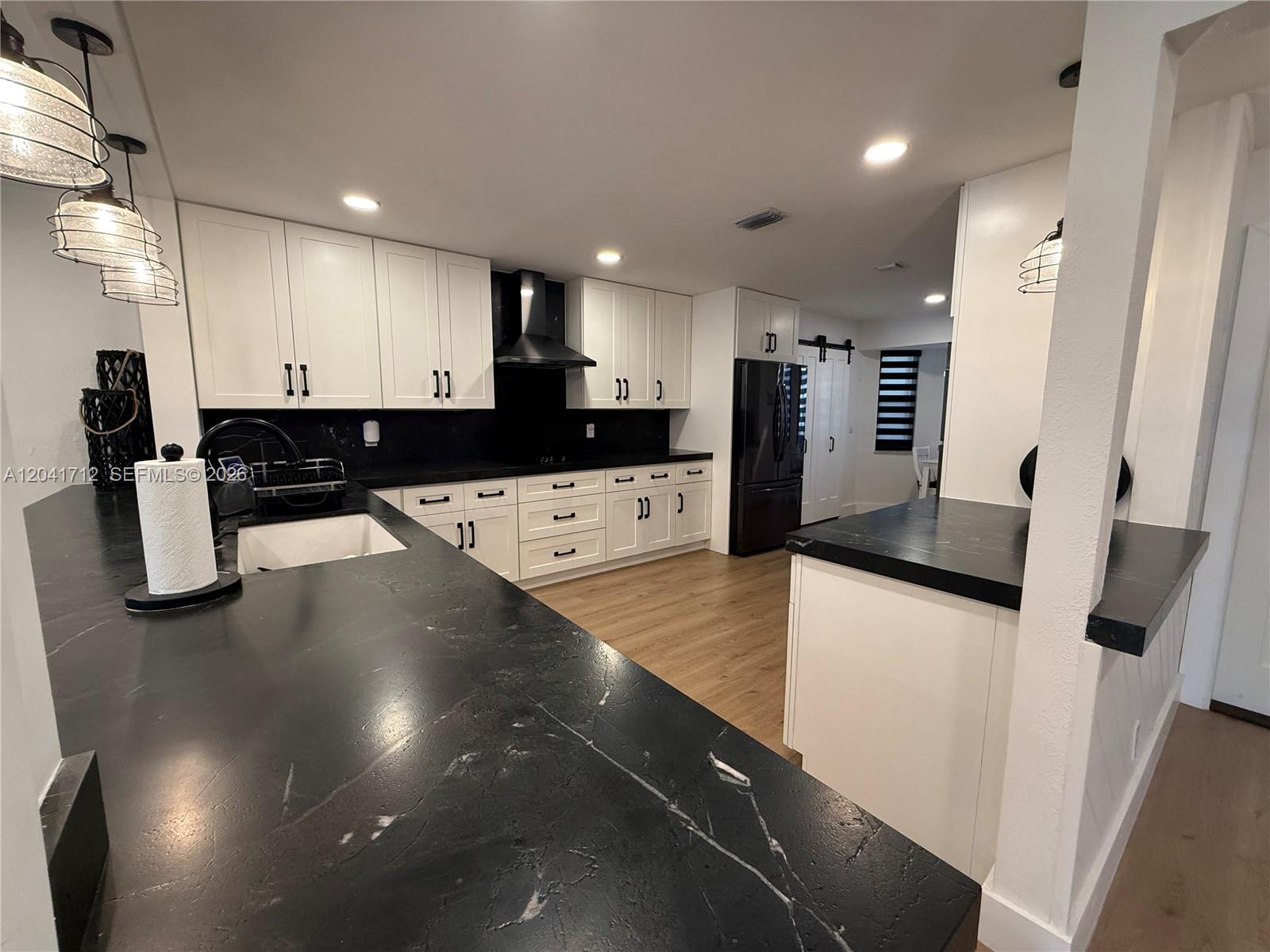 A kitchen features white cabinets, black countertops, a black range hood, and wood-look flooring — 643 Deer Creek North Shore Dr, Deerfield Beach FL 33442, DEERFIELD BEACH, FL