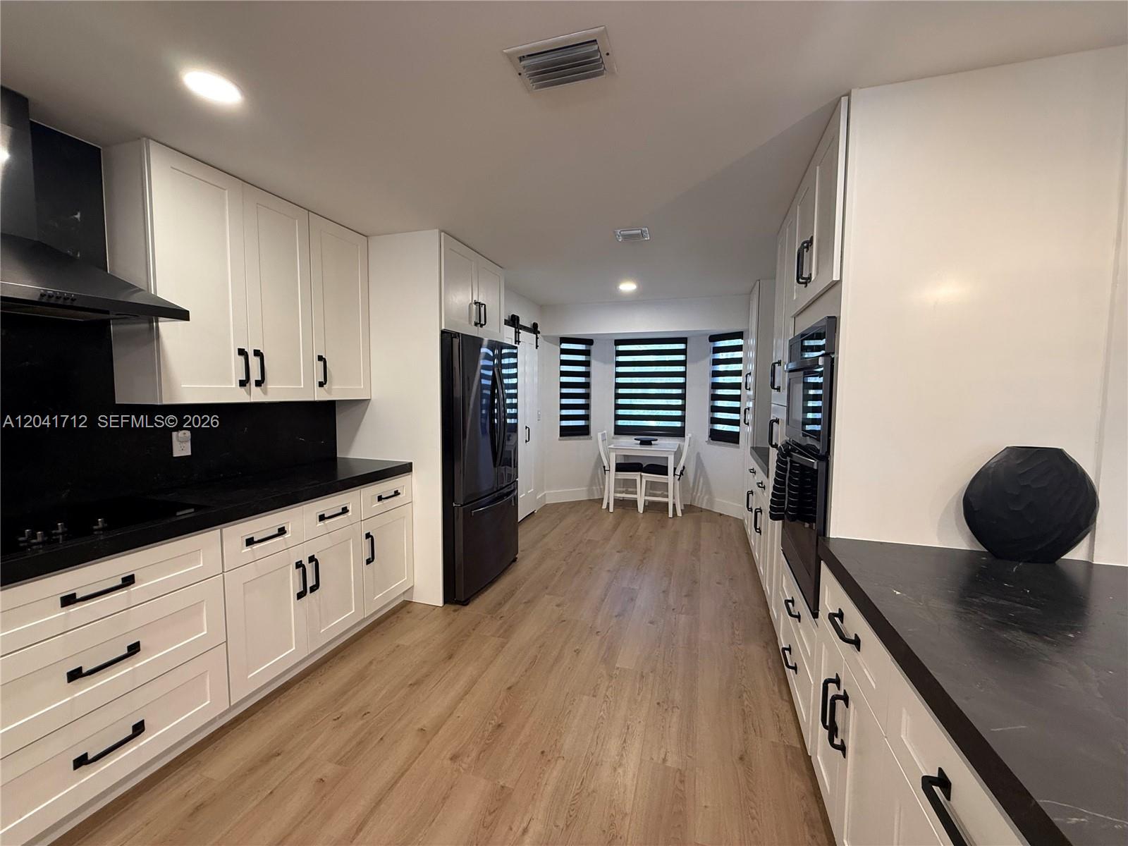 A modern kitchen features white cabinets, black countertops, stainless steel appliances, and wood-look flooring — 643 Deer Creek North Shore Dr, Deerfield Beach FL 33442, DEERFIELD BEACH, FL