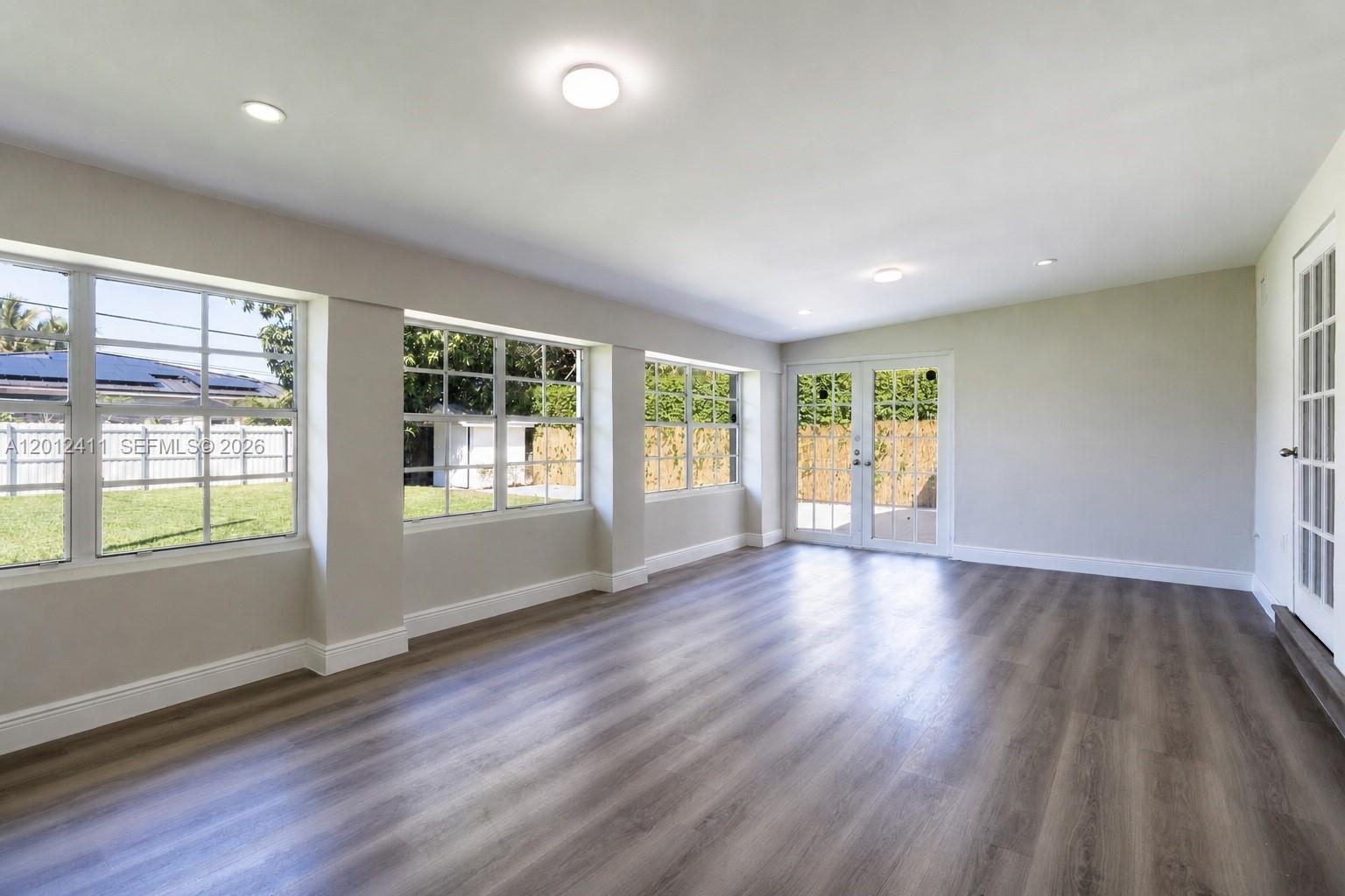 An empty room features light gray walls, wood-look flooring, multiple windows, and glass patio doors — 395 W 39th Pl, Hialeah FL 33012, HIALEAH, FL