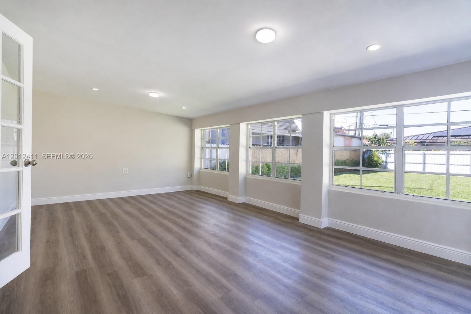 An empty room features light wood-look flooring, neutral walls, recessed lighting, and large windows — 395 W 39th Pl, Hialeah FL 33012, HIALEAH, FL
