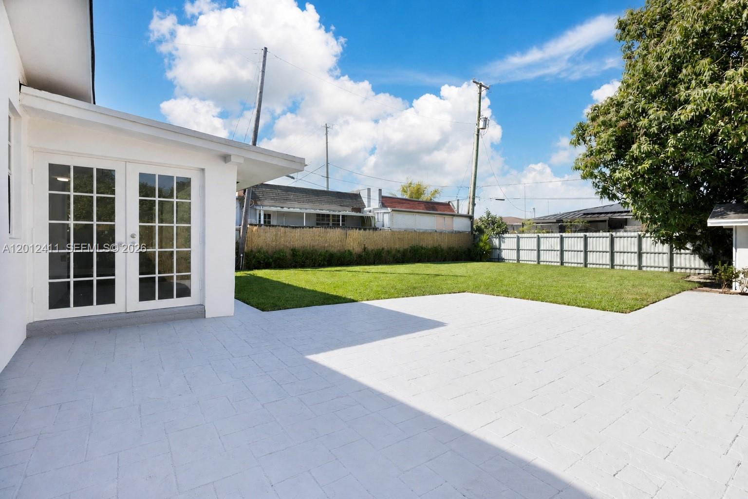 A white house with French doors opens onto a paved patio and a grassy backyard — 395 W 39th Pl, Hialeah FL 33012, HIALEAH, FL
