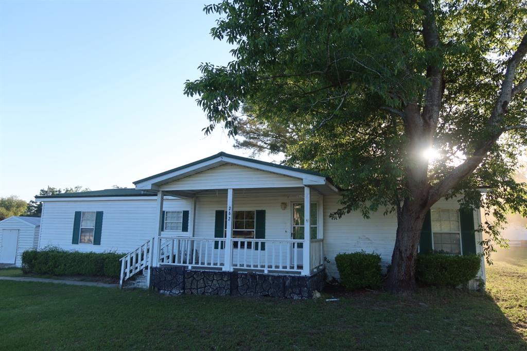 A single-story white house with a front porch and green shutters sits under a tree — 262 SW LYNNWOOD AVENUE, LAKE CITY, FL