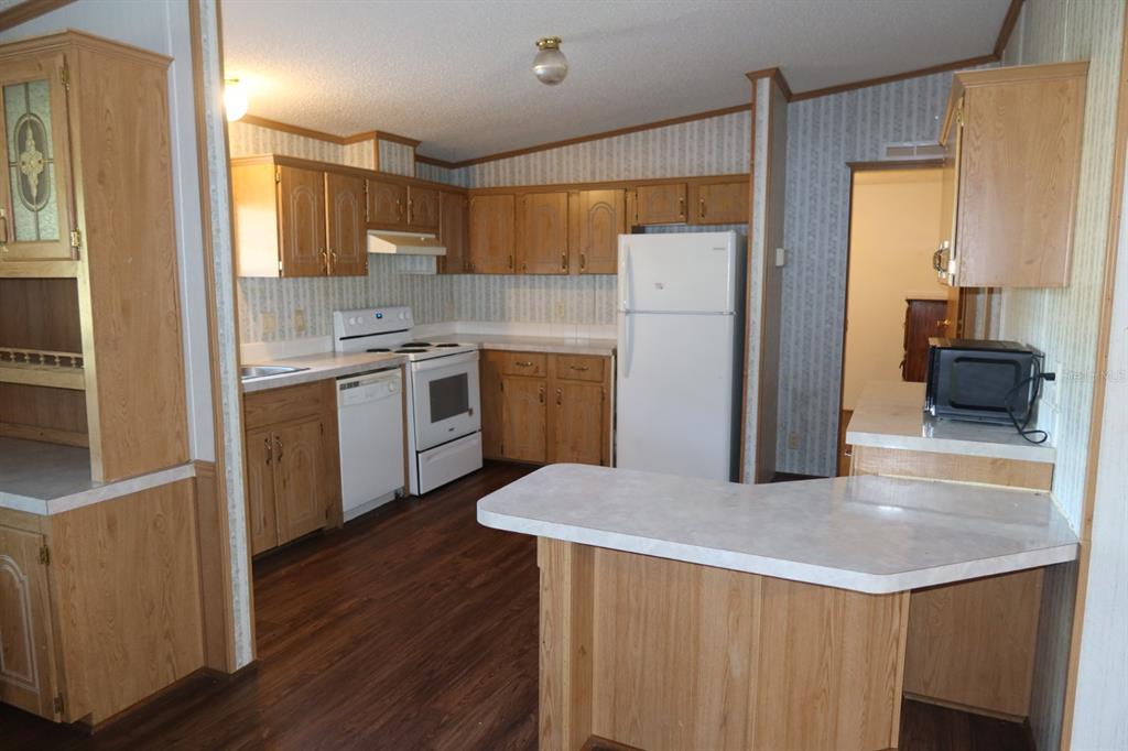A kitchen with wood cabinets, white appliances, a peninsula counter, and patterned wallpaper — 262 SW LYNNWOOD AVENUE, LAKE CITY, FL