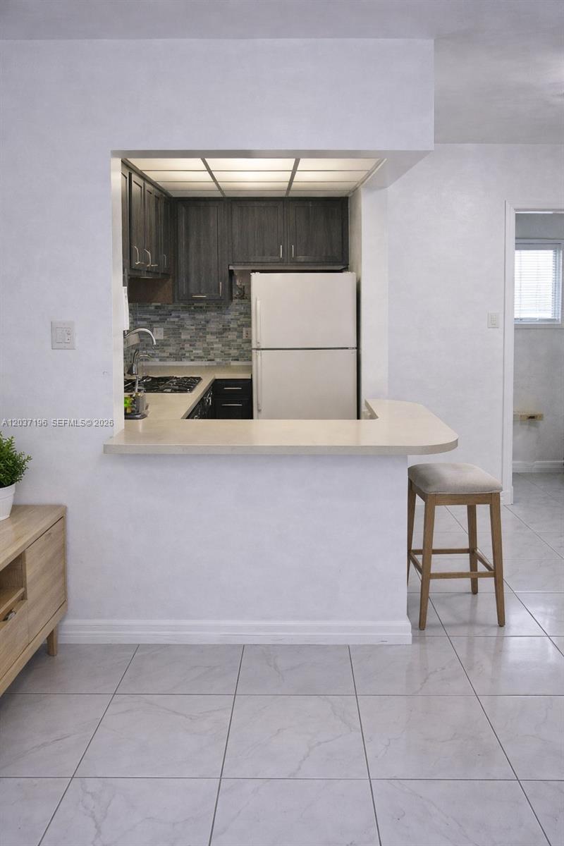 A kitchen with dark cabinets and a white refrigerator opens to a living area — 7505 SW 82nd St # 322, Miami FL 33143, MIAMI, FL