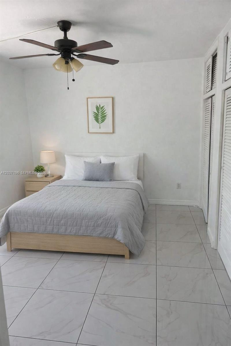 A bedroom features a bed with grey bedding, a ceiling fan, and white tiled floors — 7505 SW 82nd St # 322, Miami FL 33143, MIAMI, FL
