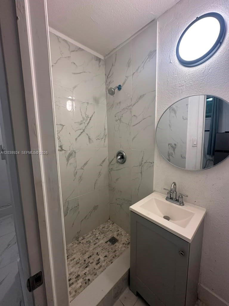 A small bathroom features a tiled walk-in shower, a pedestal sink, and a round mirror — 655 NW 2nd St # A, Florida City FL 33034, FLORIDA CITY, FL