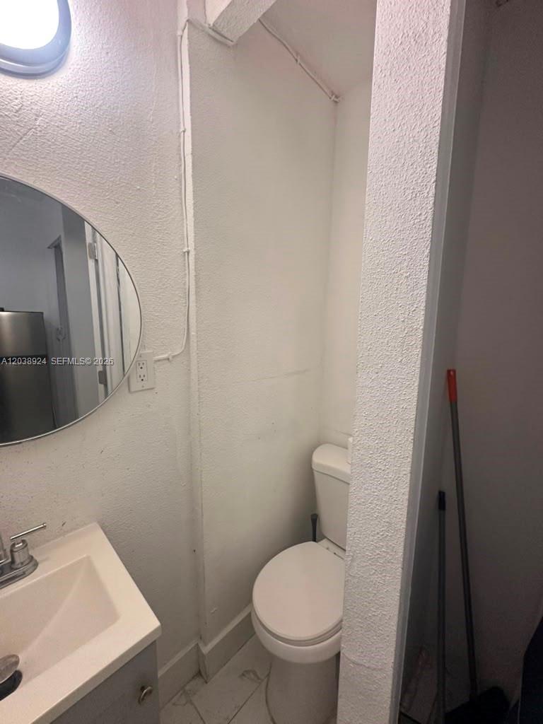 A small bathroom features a white pedestal sink, a round mirror, and a toilet — 655 NW 2nd St # A, Florida City FL 33034, FLORIDA CITY, FL
