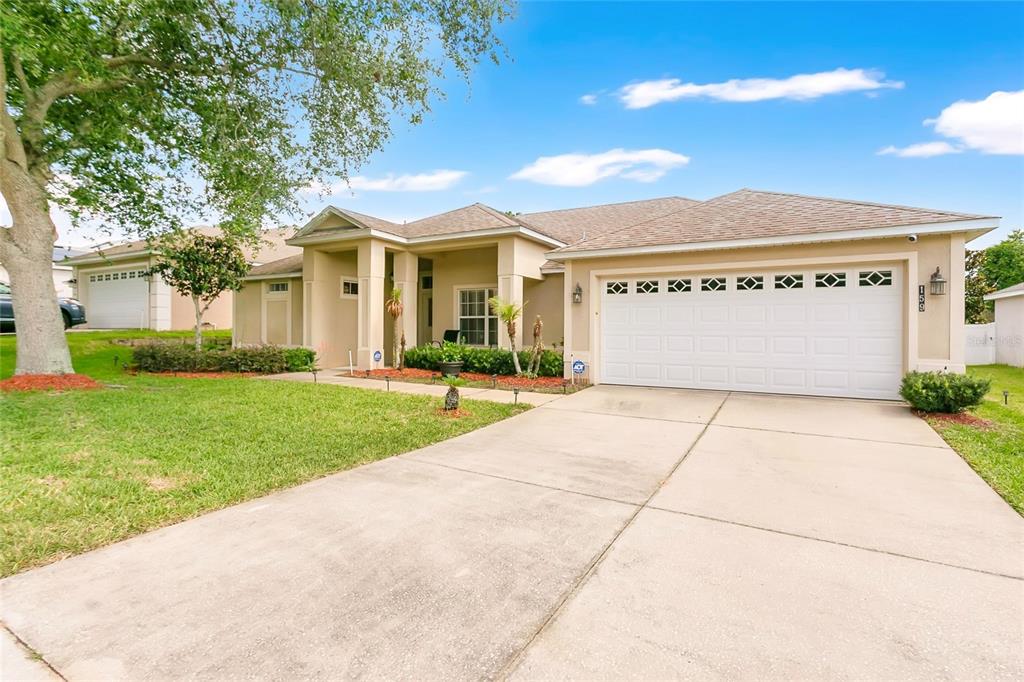 A single-story suburban house with a beige stucco exterior, a two-car garage, and a driveway — 159 COMPASS ROSE DRIVE, GROVELAND, FL