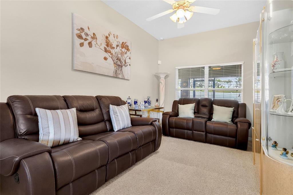 A living room features two brown leather sofas, a ceiling fan, and a glass display cabinet — 159 COMPASS ROSE DRIVE, GROVELAND, FL
