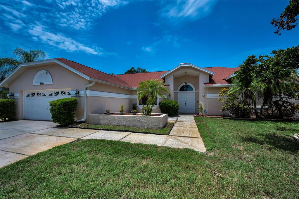 A single-story house with a beige stucco exterior, red roof, and a front walkway — 2551 INDIGO DRIVE, DUNEDIN, FL