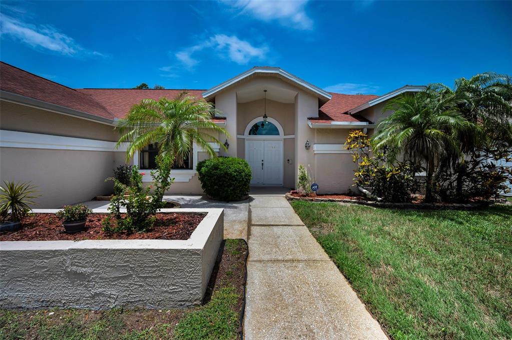 A single-story house with a beige stucco exterior, a red shingled roof, and a palm tree — 2551 INDIGO DRIVE, DUNEDIN, FL