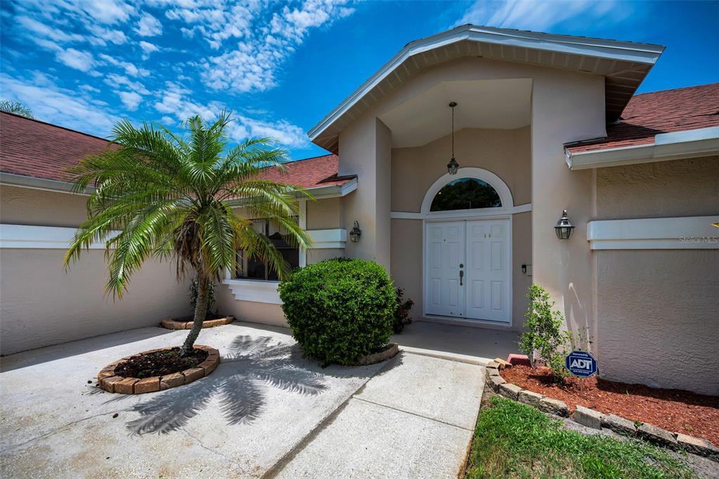 The exterior of a beige house features a palm tree, a walkway, and double doors — 2551 INDIGO DRIVE, DUNEDIN, FL