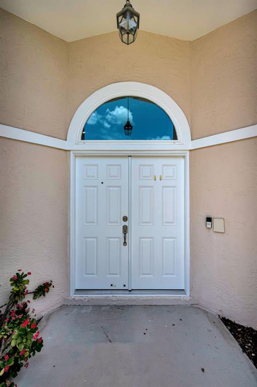 A white double front door with an arched transom window sits under a hanging light fixture — 2551 INDIGO DRIVE, DUNEDIN, FL