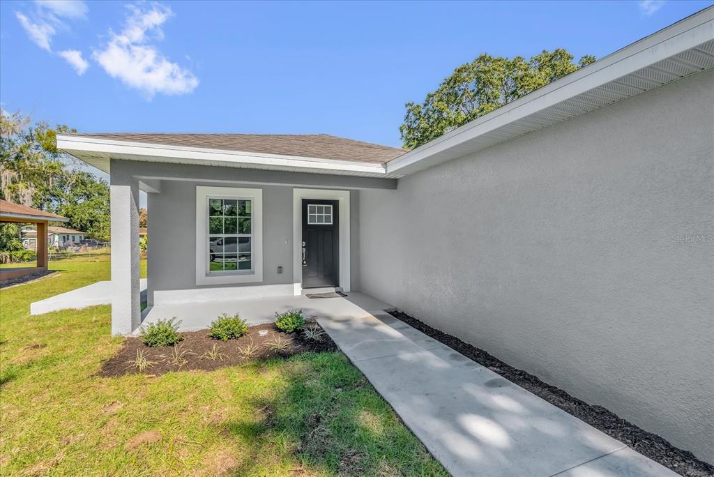 A gray house exterior features a covered entryway, a black front door, and a walkway — 1212 W 16TH STREET, SANFORD, FL