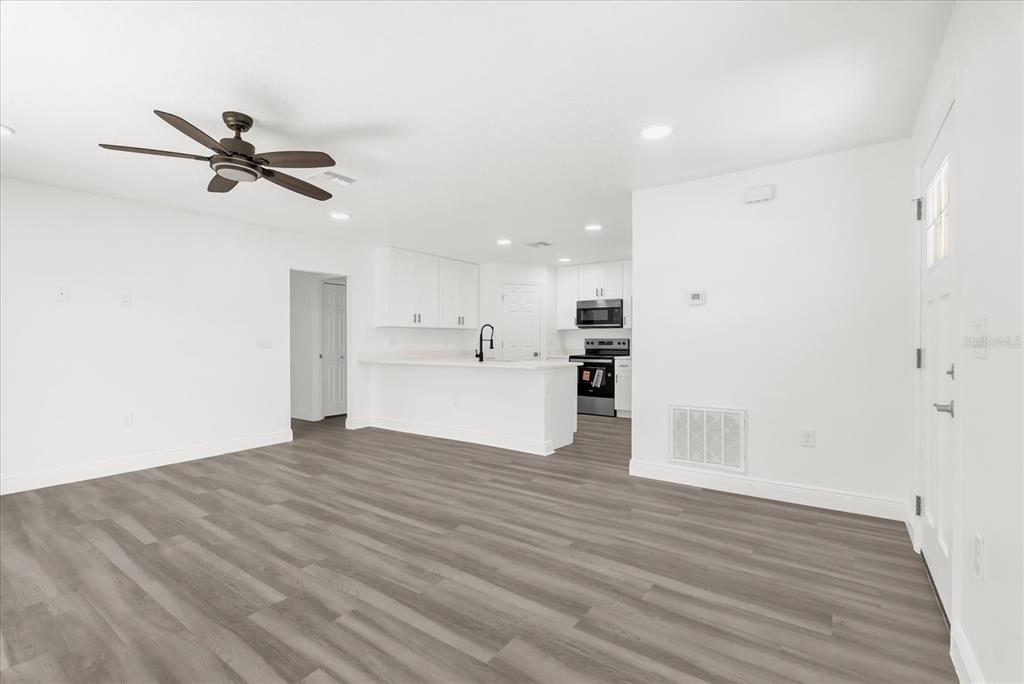 A bright, open-concept living room and kitchen area with white walls and gray wood flooring — 1212 W 16TH STREET, SANFORD, FL