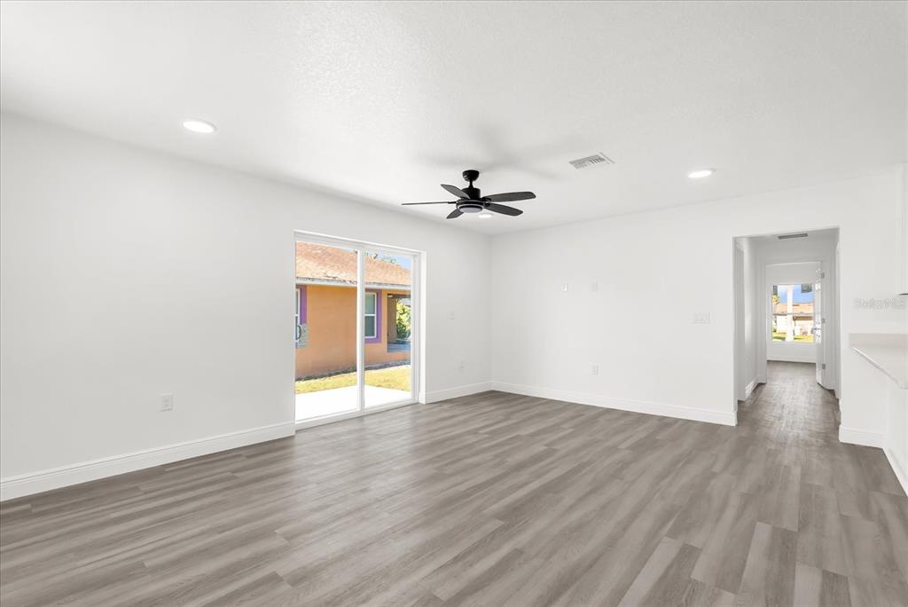 A bright living room features white walls, wood-look flooring, a ceiling fan, and sliding doors — 1212 W 16TH STREET, SANFORD, FL