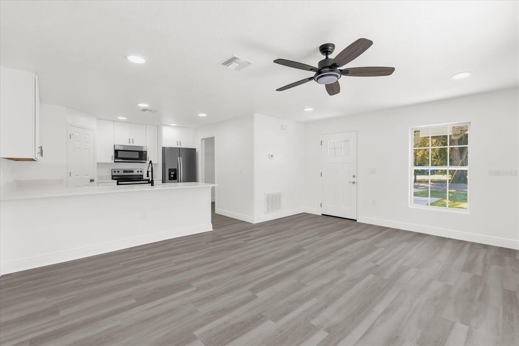 An open-concept living area features a kitchen with white cabinets and gray wood-look flooring — 1212 W 16TH STREET, SANFORD, FL