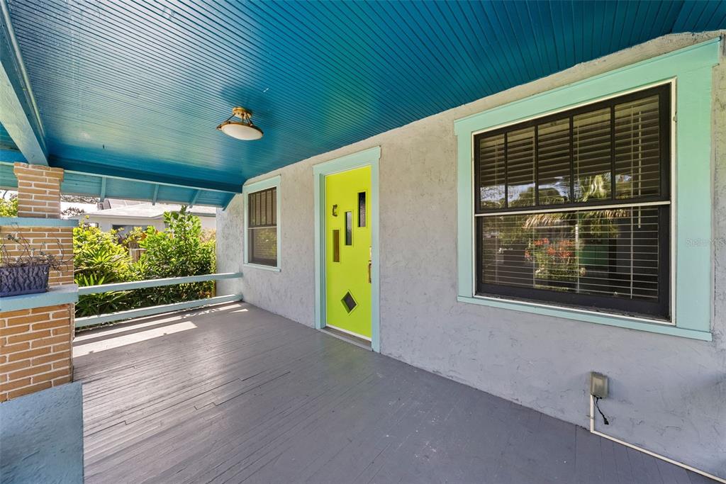 A covered front porch features a bright lime green door, gray flooring, and a blue ceiling — 1024 23RD AVENUE N, ST PETERSBURG, FL