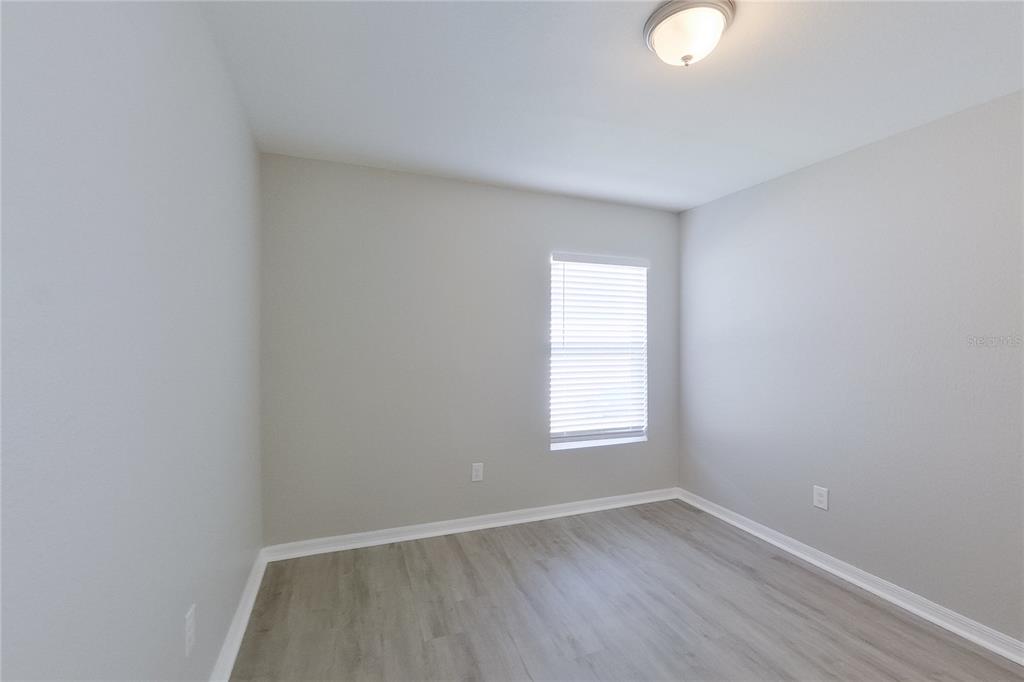 An empty room features light gray walls, white trim, and wood-look flooring — 18310 GIBRALTAR LANE, LEHIGH ACRES, FL