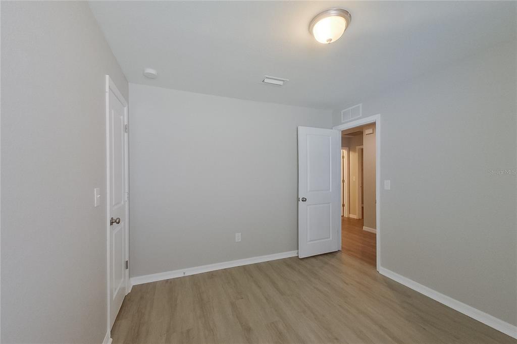 An empty bedroom features light gray walls, wood-look flooring, and two white interior doors — 18310 GIBRALTAR LANE, LEHIGH ACRES, FL