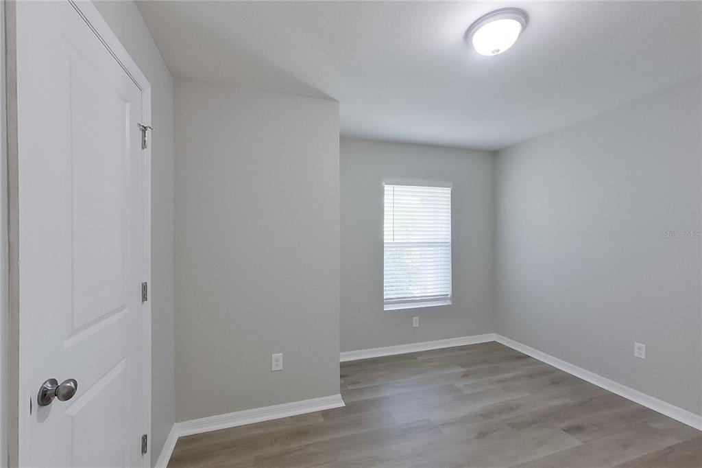 An empty bedroom features light gray walls, wood-look flooring, a window, and a ceiling light — 18310 GIBRALTAR LANE, LEHIGH ACRES, FL