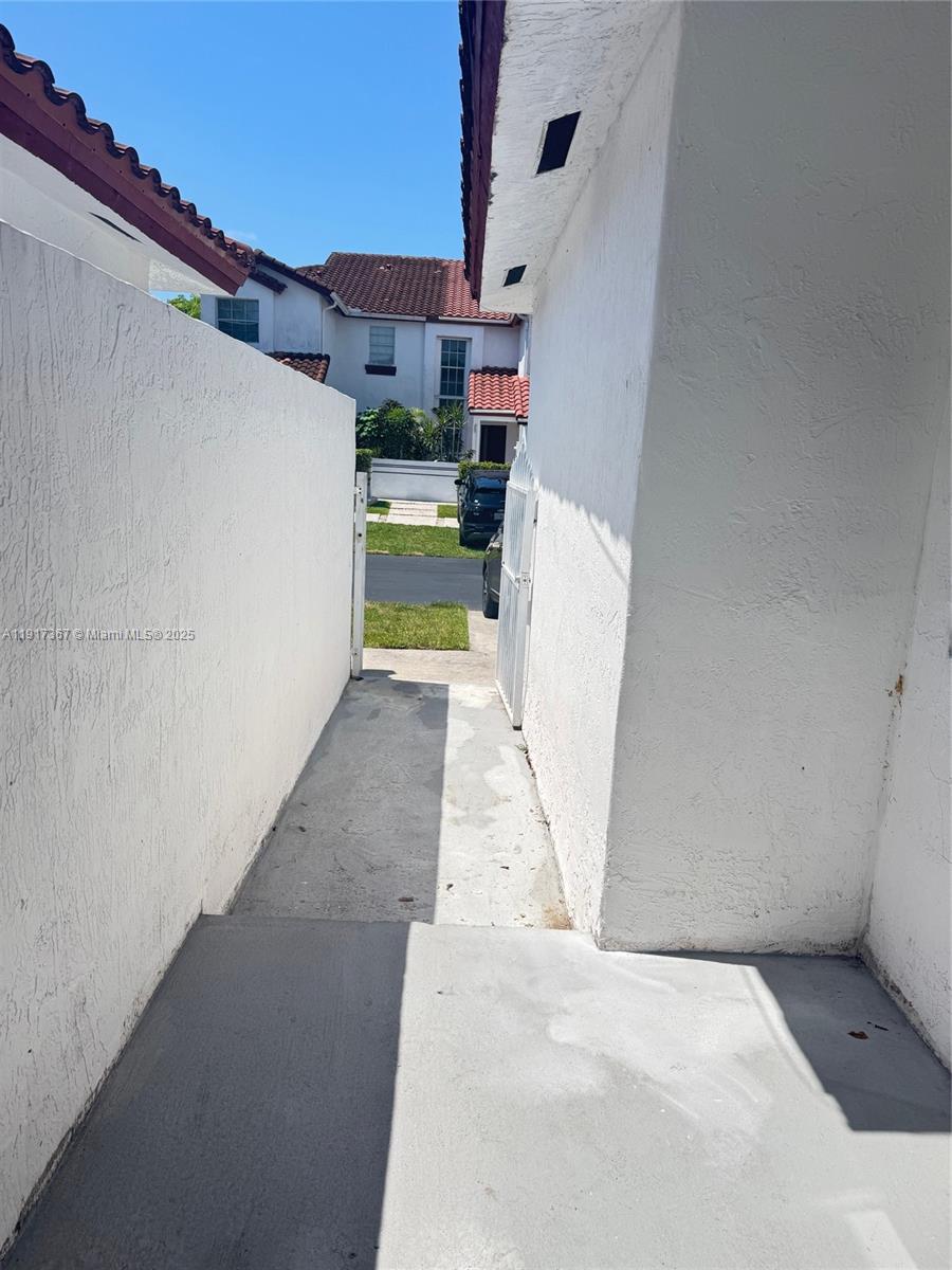 A narrow concrete walkway leads between two white stucco walls toward a residential street — 8419 SW 209th St, Cutler Bay FL 33189, CUTLER BAY, FL