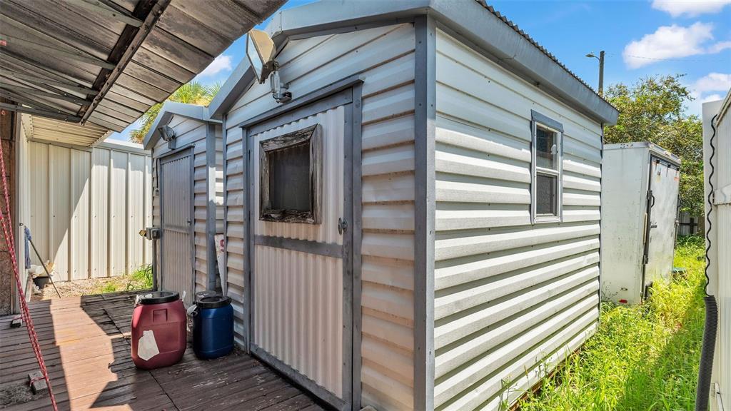 A small, light-colored metal shed sits on a wooden deck next to a storage trailer — 2999 US HIGHWAY 92, WINTER HAVEN, FL
